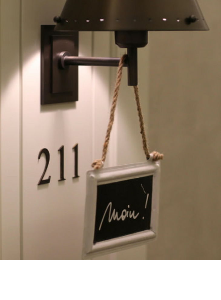 Türschild mit Zimmernummer 211 und kleinem Schild "Moin!" an einer Wandlampe im Severin*s Resort & Spa, Sylt.