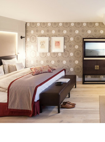 Elegant hotel room with double bed, decorative cushions, stylish wallpaper and artwork on the wall.