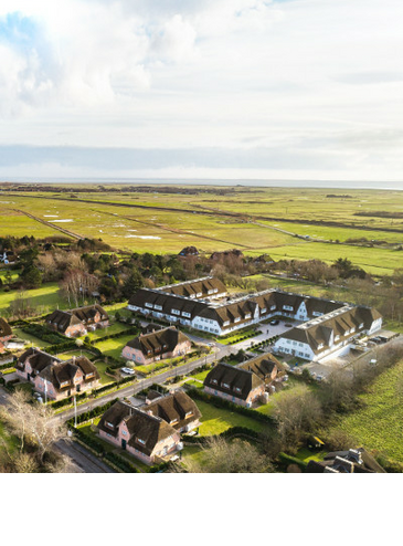Aerial view of the Severin*s Resort & Spa on Sylt, surrounded by green meadows and thatched-roof houses.