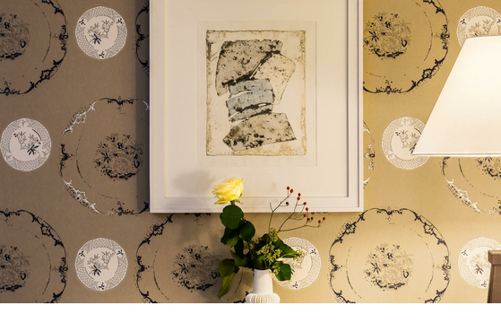 Kunstwerk an gemusterter Tapete, daneben Tischlampe und Vase mit gelber Rose im Severin*s Resort & Spa auf Sylt.