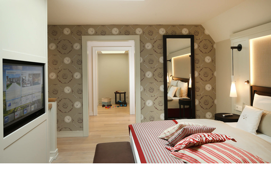 Luxuriöses Hotelzimmer mit Doppelbett, stilvollen Tapeten, modernen Leuchten und Blick auf ein angrenzendes Spielzimmer.