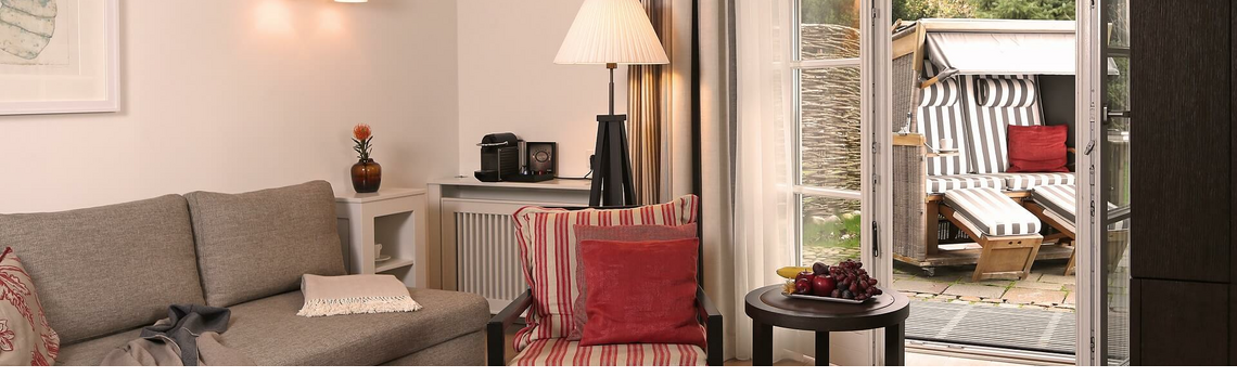Gemütliches Wohnzimmer mit Sofa, Sessel, Couchtisch, Lampe und Zugang zur Terrasse mit Strandkorb im Severin*s Resort & Spa.