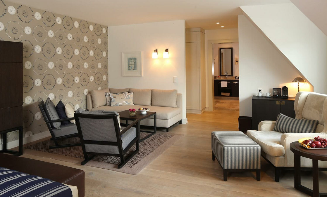 Elegantes Hotelzimmer mit gemütlicher Sitzecke, stilvoller Tapete und modernem Bad im Severin*s Resort & Spa auf Sylt.