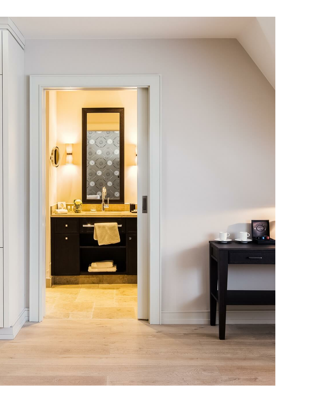 Helles Hotelzimmer mit Blick ins stilvolle Bad, Schreibtisch mit Kaffeemaschine und Lampe, elegante Einrichtung.