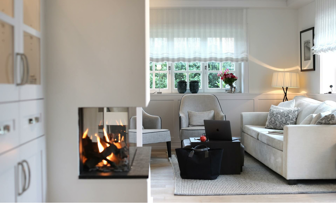 Elegantes Wohnzimmer mit Kamin, gemütlicher Sitzecke, Laptop auf Couchtisch, großen Fenstern und stilvoller Beleuchtung.