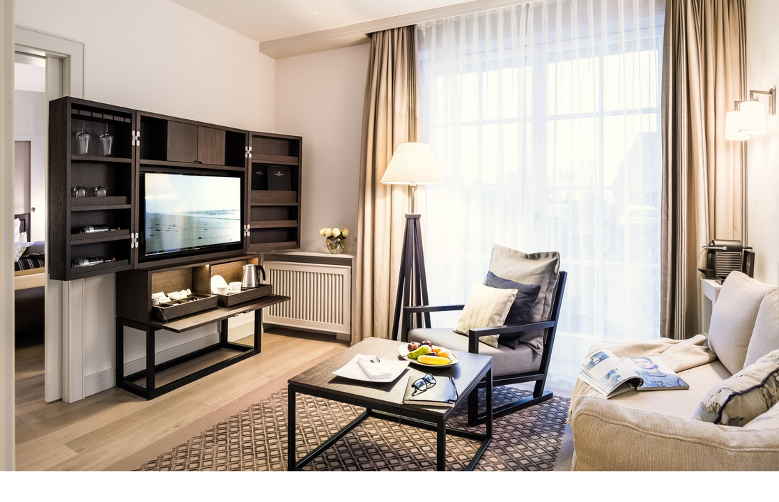 Elegant living room at Severin*s Resort & Spa Sylt with sofa, armchair, TV, coffee table and large windows.