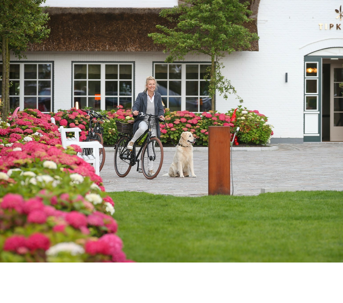 Frau mit Hund und Fahrrad vor dem Severin*s Resort & Spa, umgeben von blühenden Hortensien.