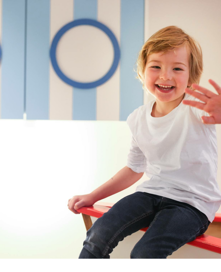 Fröhliches Kind im Kids Club des Hotel Severin*s auf Sylt Lachendes Kind auf roter Bank im kinderfreundlichen Bereich des Severin*s Resort & Spa, Sylt.