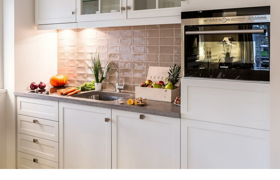 Modern hotel kitchen with white cupboards, fruit, vegetables and built-in oven.