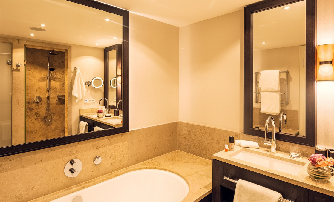 Luxuriöses Badezimmer mit großer Badewanne, Doppelwaschbecken, Spiegeln und eleganter Beleuchtung im Severin*s Resort.