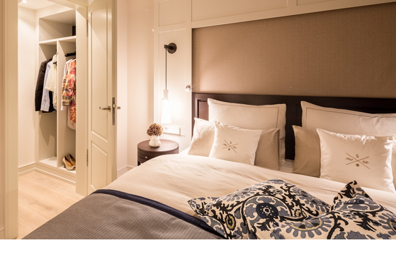 Elegant hotel room with cozy bed, fine bed linen, stylish pillows and open closet in the background.
