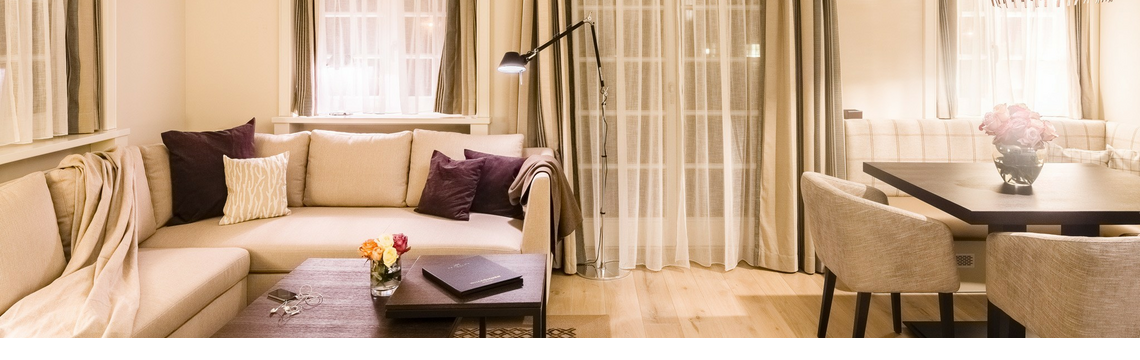 Elegant living room at Severin*s Resort & Spa with beige sofa corner, stylish dining table and subtle lighting.