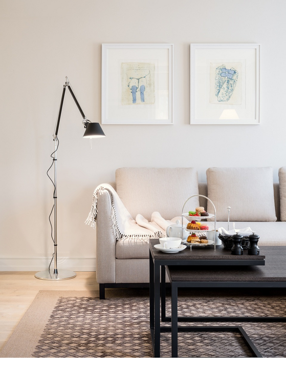 Elegant living room with beige sofa, floor lamp, artwork on the wall and a table with tea and cookies.