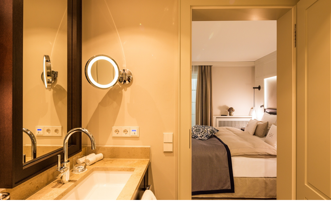 Luxuriöses Hotelzimmer mit elegantem Bad, stilvollem Waschbecken und gemütlichem Bett, warm beleuchtet.