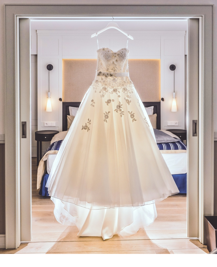 Elegant wedding dress hangs in luxurious hotel room with stylish furnishings and soft lighting.