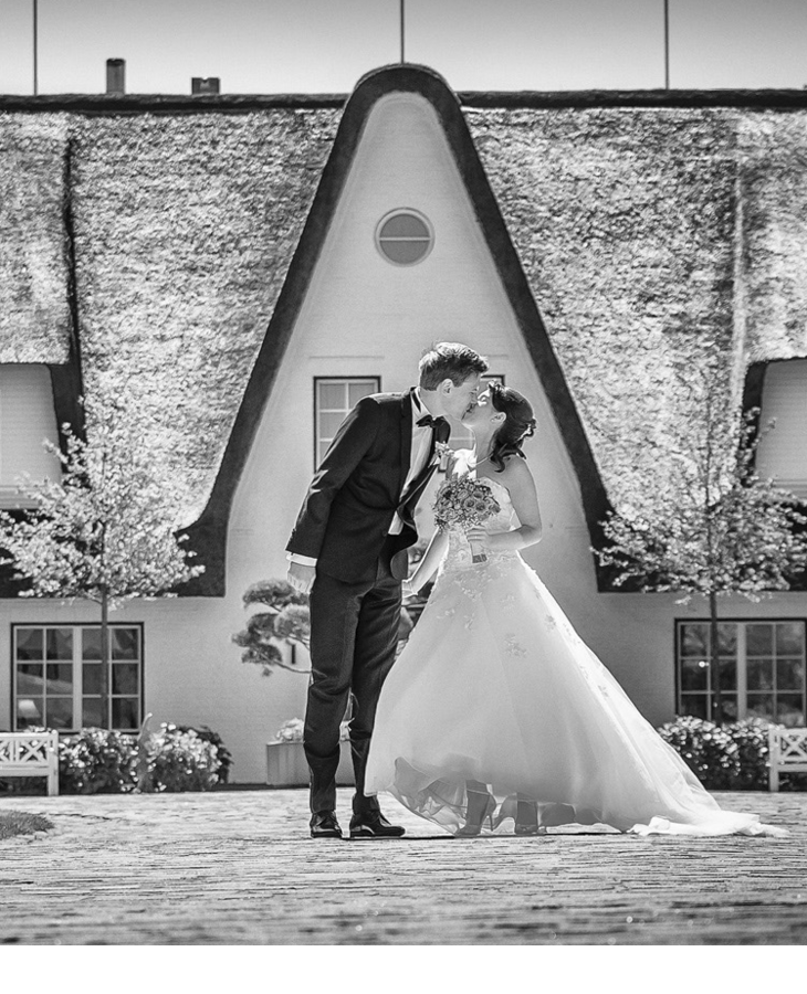Braut und Bräutigam Kuss vor dem Hauptgebäude des Hotel Severin*s Resort und Spa auf Sylt Bridal couple kissing in front of the thatched Severin*s Resort & Spa on Sylt.
