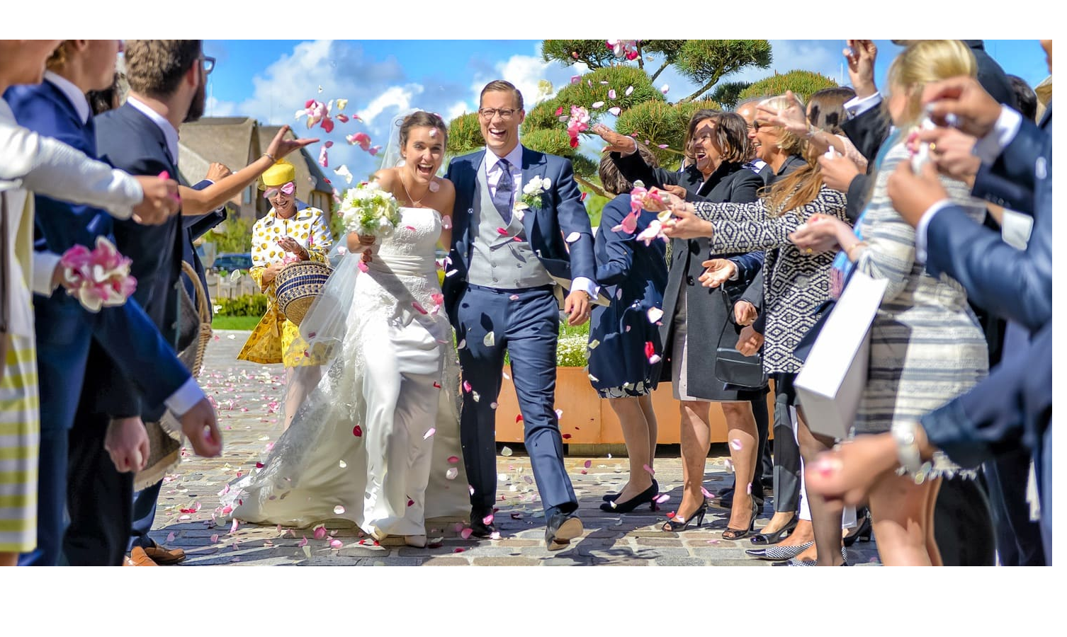 Wedding couple under a blue sky, guests throwing petals, festive atmosphere at Severin*s Resort & Spa on Sylt.