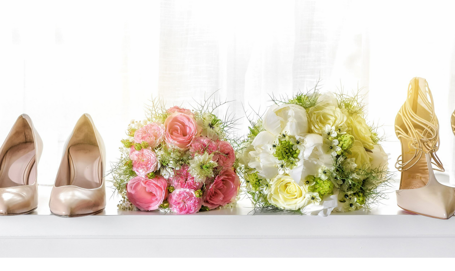Two pairs of elegant women's shoes and two bouquets of flowers, pink and white, on a windowsill.