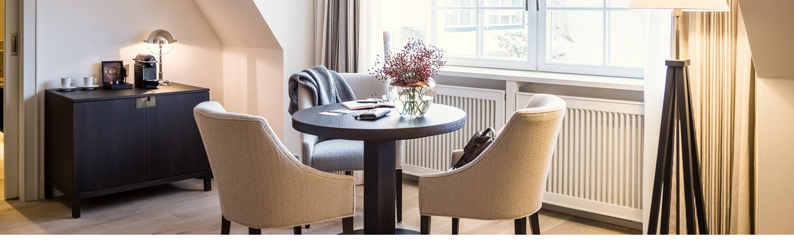 Cozy sitting area with table, two armchairs, floor lamp and window at Severin*s Resort & Spa on Sylt.
