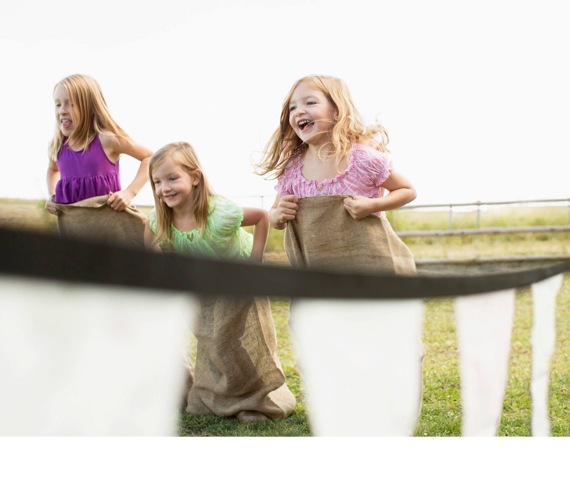 Spielende Kinder im Kids Club des Hotel Severin*s Resort und Spa auf Sylt Drei lachende Kinder beim Sackhüpfen auf einer Wiese im Severin*s Resort & Spa auf Sylt.