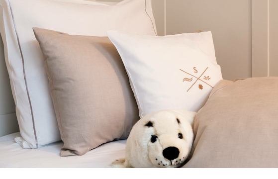 Luxurious bed with white and beige pillows, decorated with a plush seal, at Severin*s Resort & Spa on Sylt.
