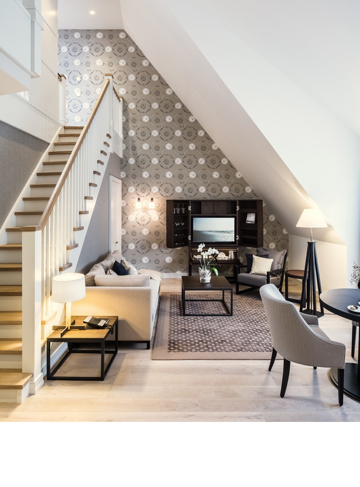 Living area and stairs in Maisonette Senior Suite in Hotel Severin*s on Sylt Elegant living room with staircase, sofa, TV, carpet and stylish furniture at Severin*s Resort & Spa on Sylt.