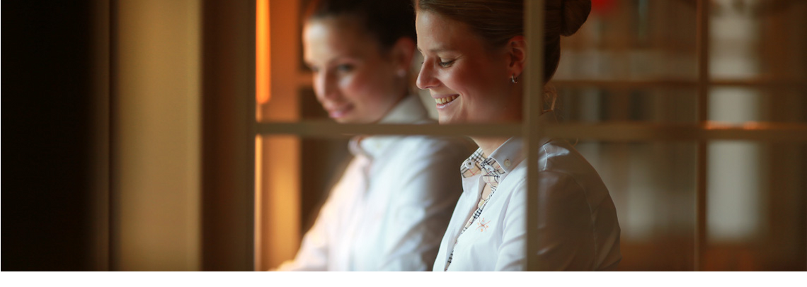 Service Severin*s Resort & Spa Hotel employee in white uniform smiles friendly behind a glass wall at Severin*s Resort & Spa on Sylt.