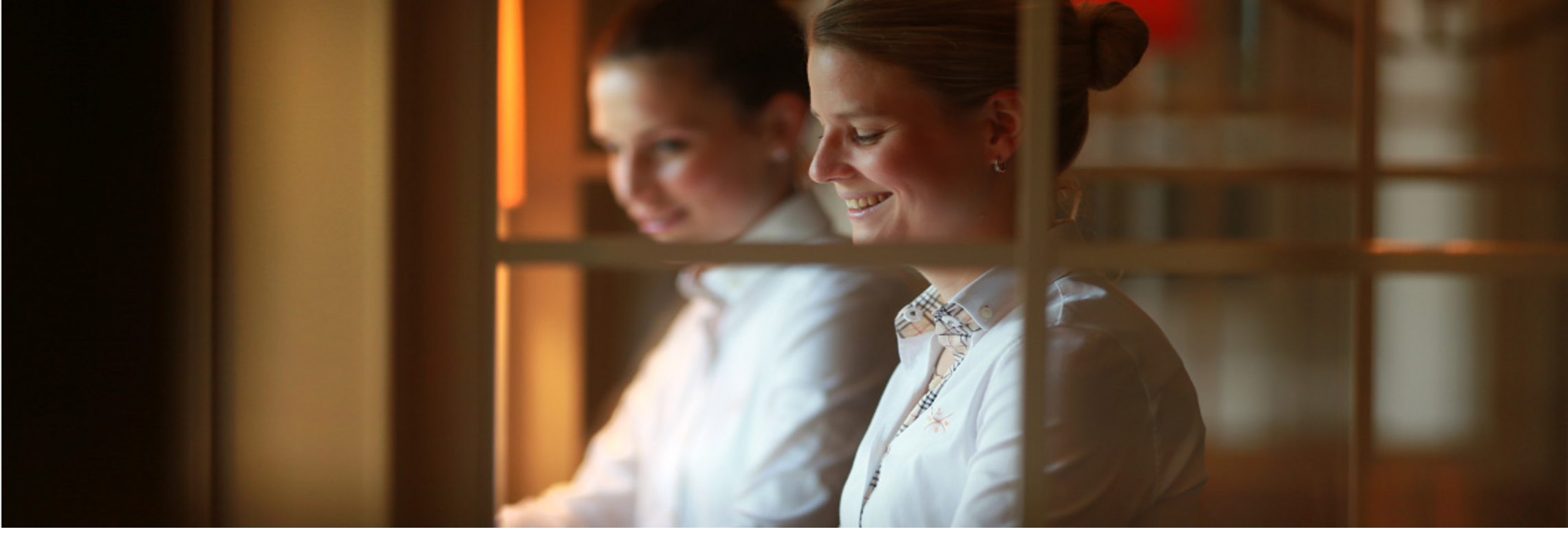 Hotelmitarbeiterin in weißer Uniform lächelt freundlich hinter Glaswand im Severin*s Resort & Spa auf Sylt.