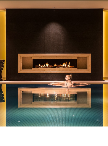 A young woman bathes in the swimming pool with fireplace and relaxation area of ​​the Severin*s Resort and Spa on Sylt