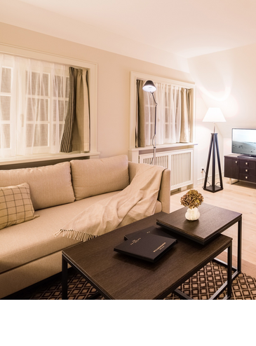 Korblampe im Wohnzimmer des Studios im Hotel Severin*s Resort und Spa auf Sylt Elegante Suite mit gemütlichem Sofa, Flachbild-TV, Esstisch und stilvoller Beleuchtung im Severin*s Resort & Spa auf Sylt.