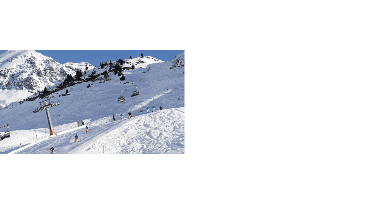 Skiers on a snowy slope with chairlift in the background, surrounded by mountains and blue sky.